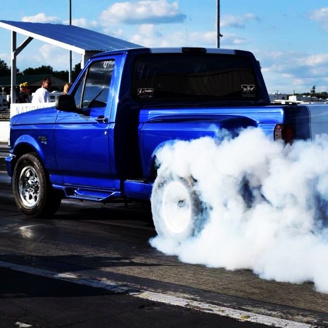 A blue high-performance diesel truck performing a burnout on a drag strip