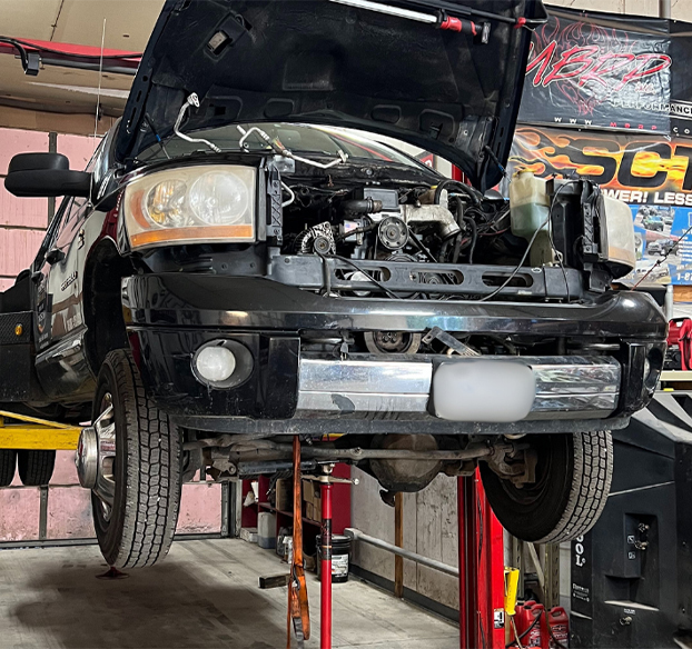 Diesel repair. Auto shop in Bremen, OH, Unlimited Diesel Performance. A black pickup truck lifted on a red hydraulic lift in a mechanic workshop with the hood open.